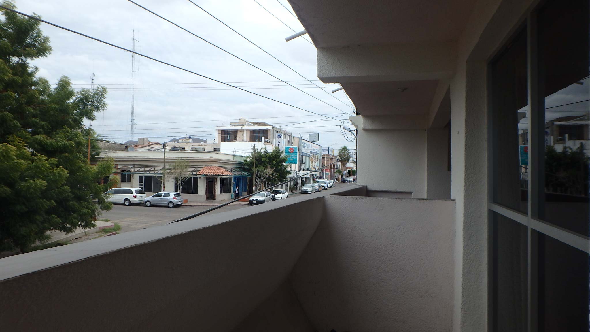 An off-white balcony wall overlooks a city street corner lined with cars.