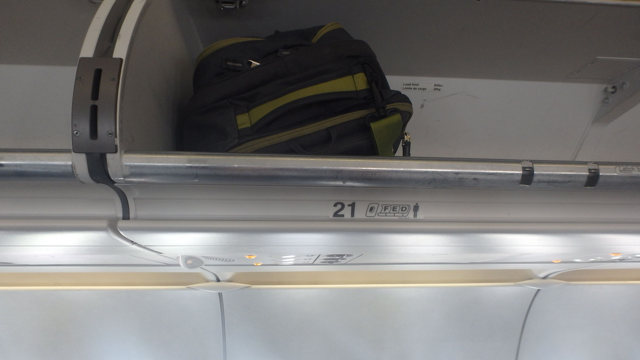 A grey and green backpack stowed neatly in an airplane's otherwise empty overhead luggage compartment.